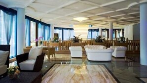 Un hall d’entrée spacieux avec un sol en marbre, des canapés blancs et des rideaux bleus.