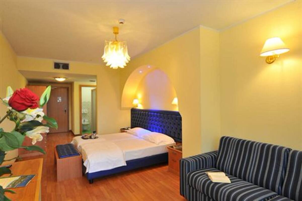 Quarto de hotel com cama, sofá, mesa de trabalho com luminária e um arranjo de flores.