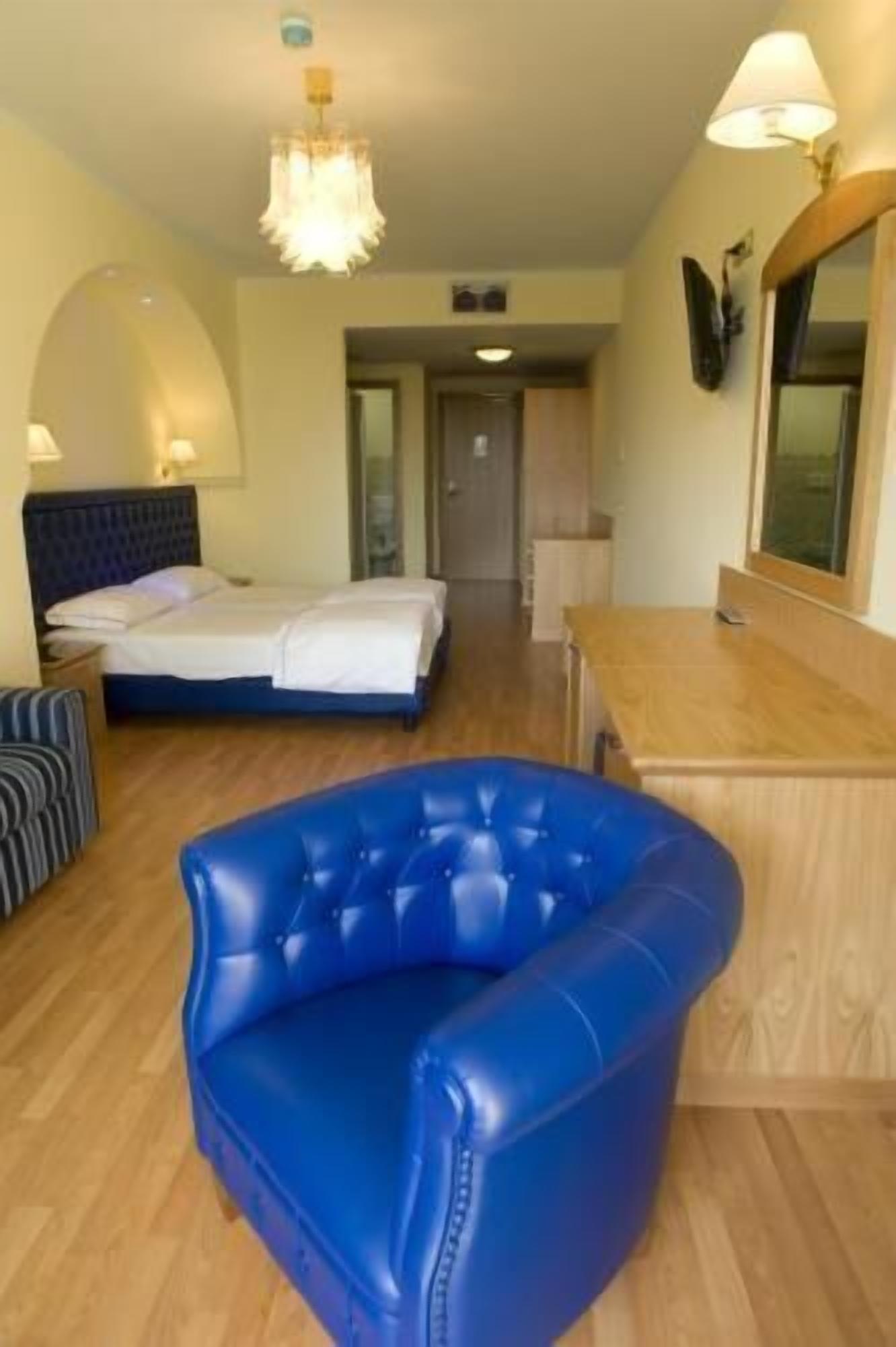 A hotel room with a bed, a blue armchair, a wooden desk, and a mirror.