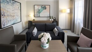 Een moderne hotelkamer met een bank, een bijzettafeltje met bloemen, een bureau en een groot schilderij aan de muur.