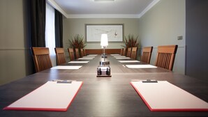 Een vergaderruimte met een lange tafel, stoelen, een beamer en een lijst in een lijstwerk op de muur.