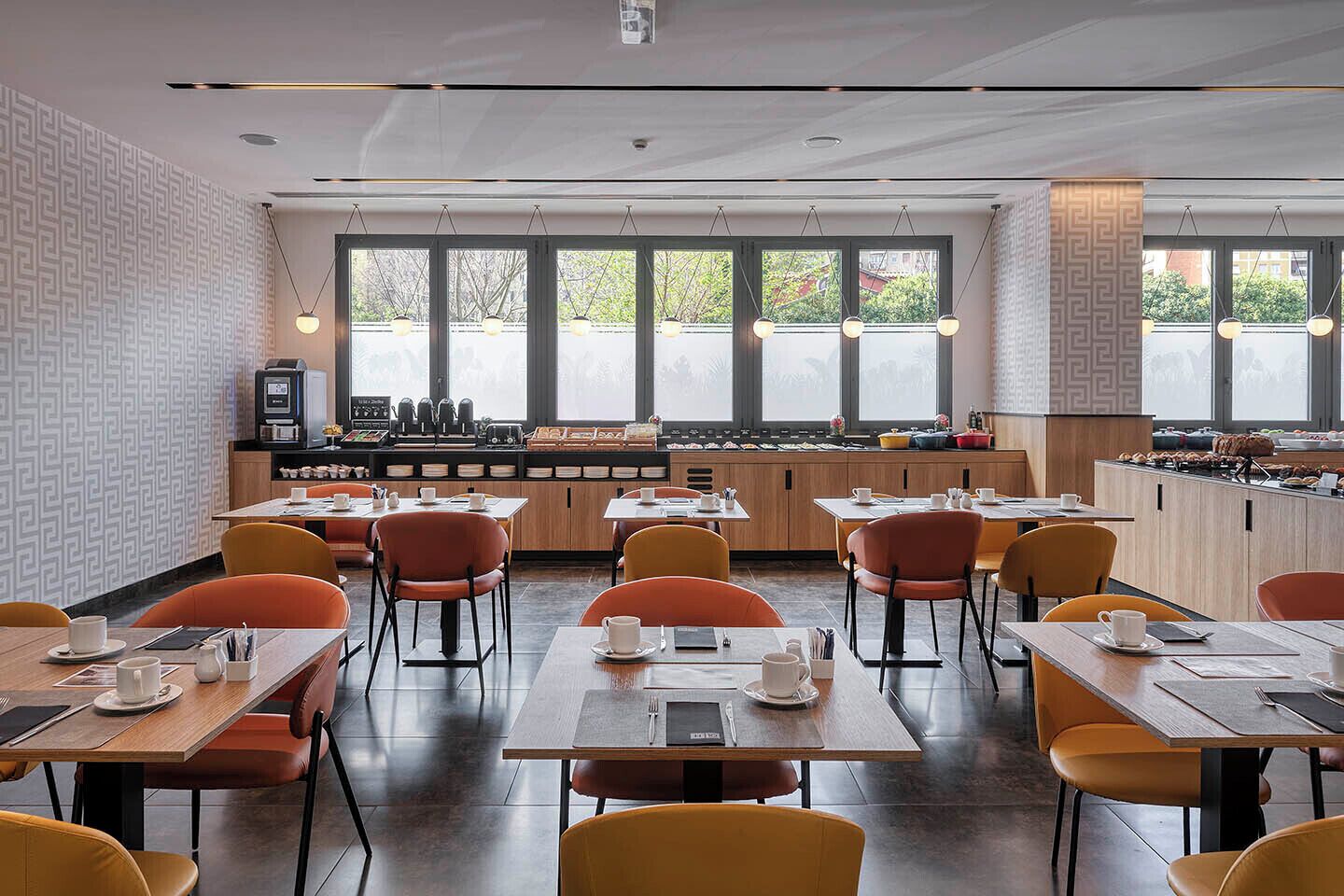 Un caffè moderno con tavoli di legno, sedie arancioni, ampie finestre e un angolo caffetteria.