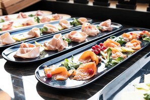A series of black rectangular plates with various food items, including salmon and vegetables, arranged on a reflective surface.