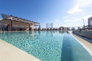 A swimming pool with clear water, sun loungers, and a covered seating area.