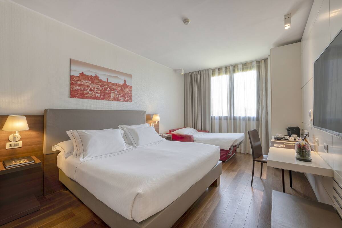 A hotel room with a large bed, a desk, a chair, and a TV.