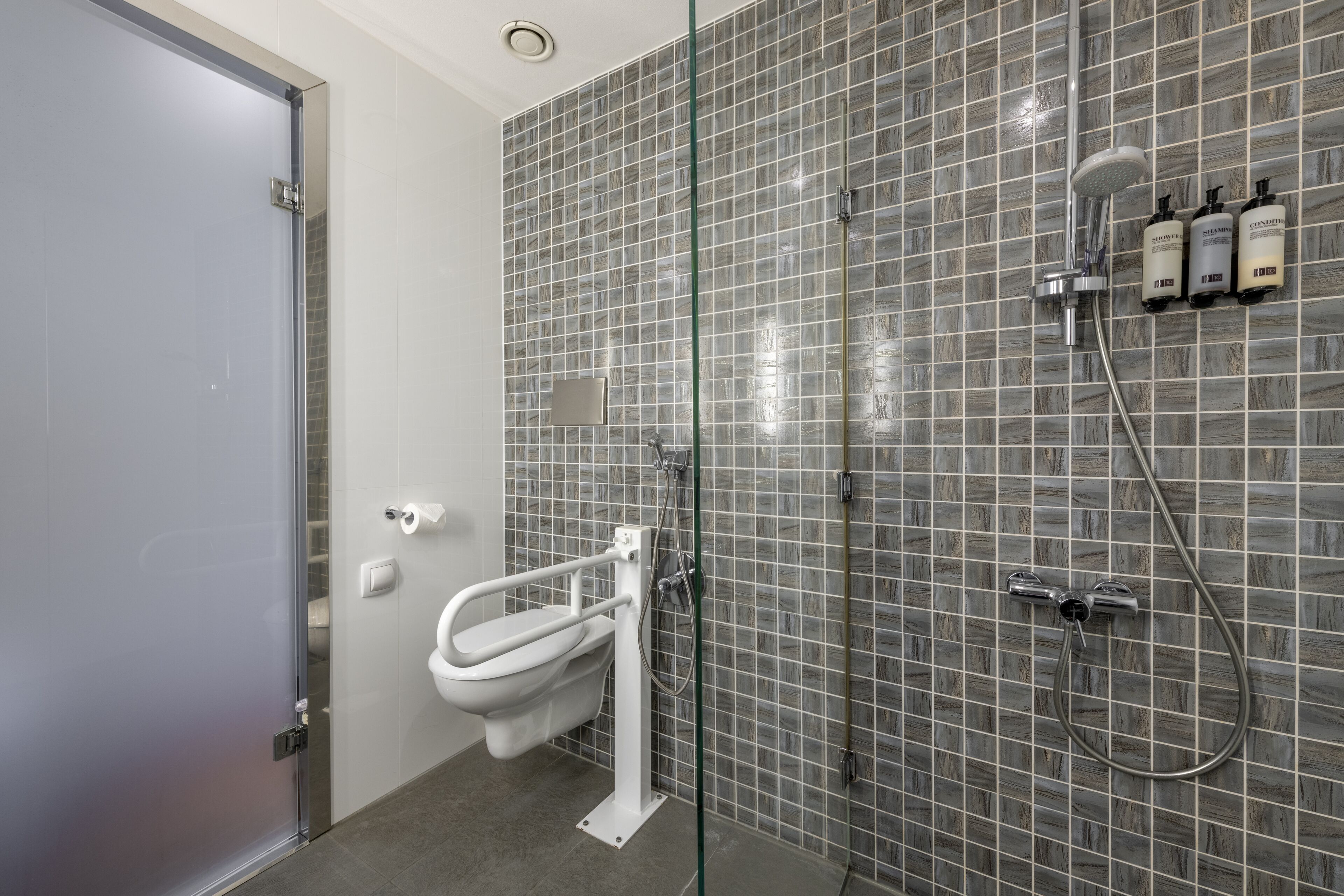 A modern bathroom with a glass partition, a white toilet, a shower area, and three bottles of shampoo on the wall.
