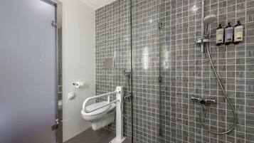 A modern bathroom with a glass partition, a white toilet, a shower area, and three bottles of shampoo on the wall.