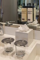 Un bagno con uno specchio, un lavandino e due contenitori di vetro vuoti con etichette.