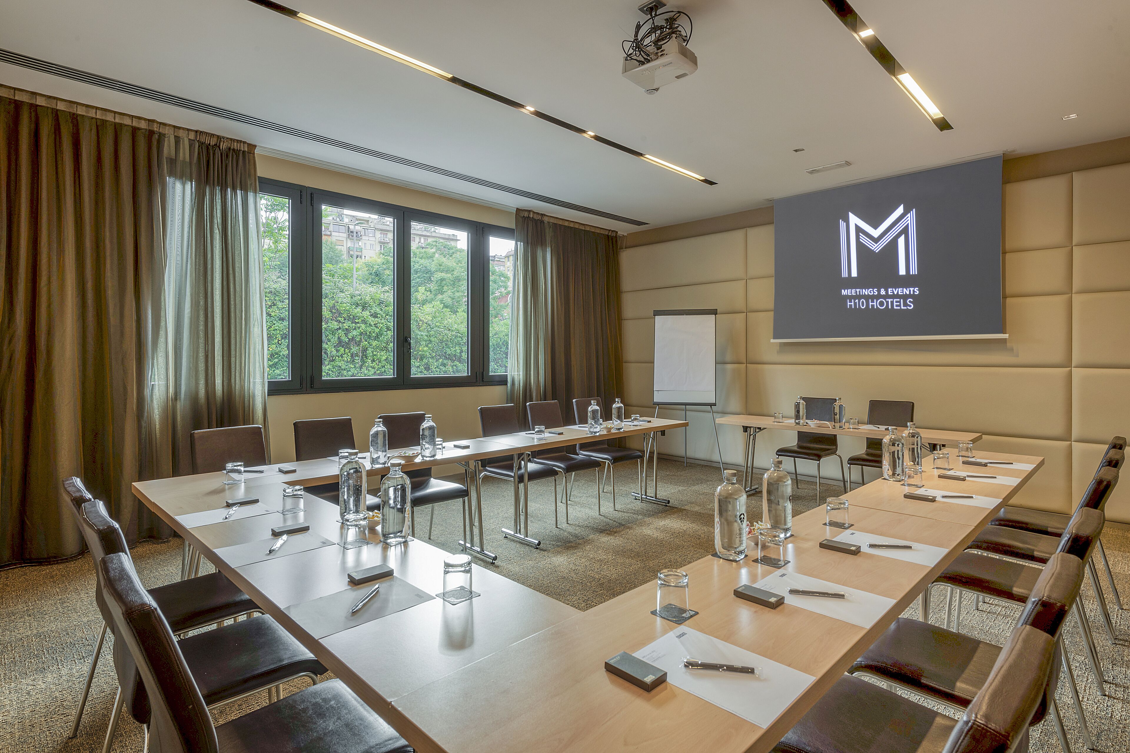 Un salón de conferencias con una larga mesa, sillas y una pantalla de proyector que muestra el logotipo del hotel.