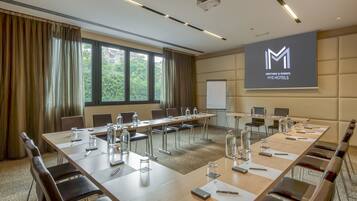 Un salón de conferencias con una larga mesa, sillas y una pantalla de proyector que muestra el logotipo del hotel.