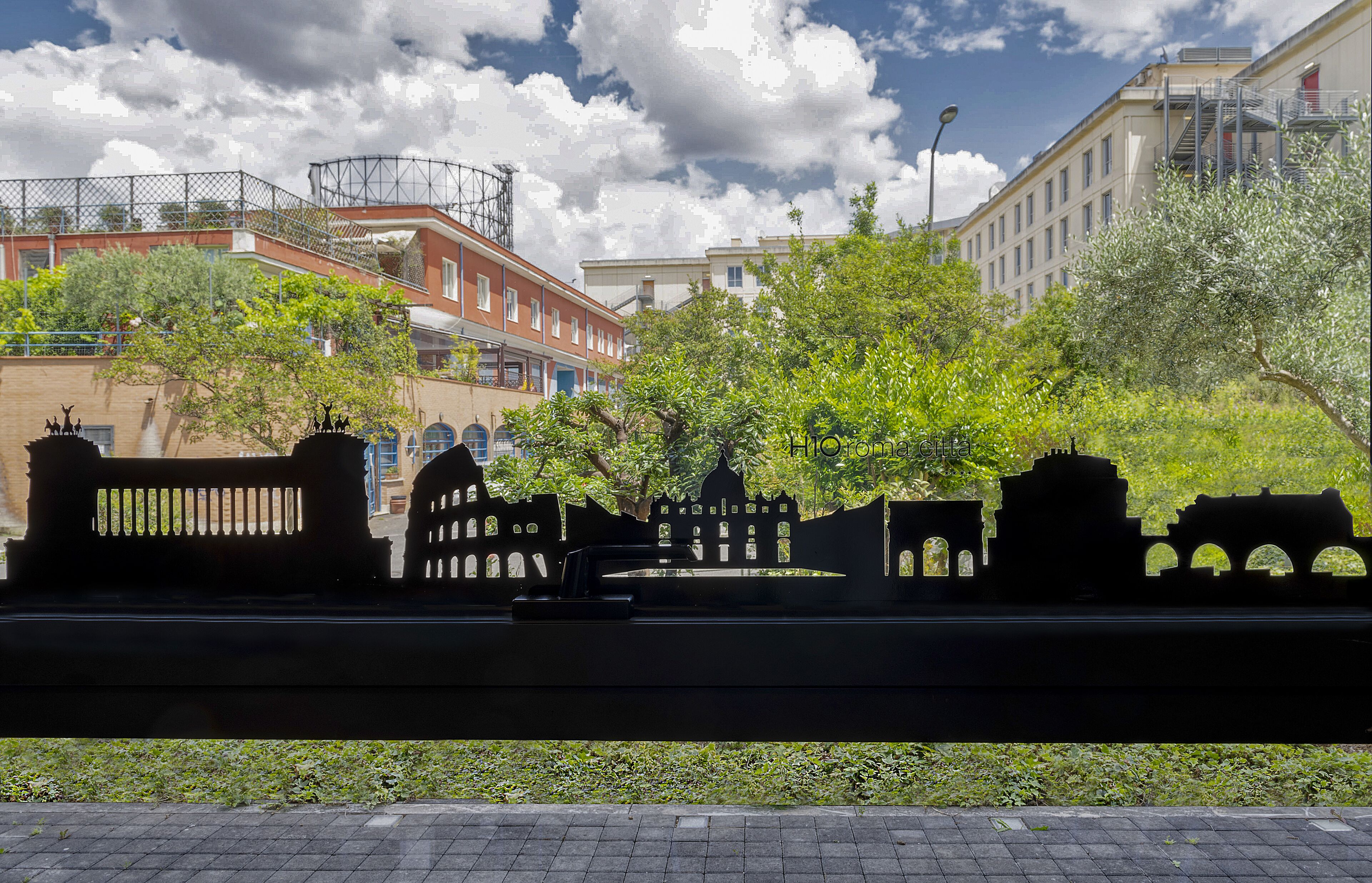 Vista de una calle con una valla de metal, árboles y edificios al fondo.
