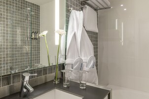 Un bagno moderno con cabina doccia in vetro, uno specchio grande e un mobile lavabo con lavandino e due bottiglie di vetro trasparente.