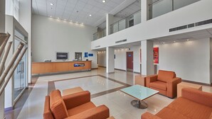 Un vestíbulo amplio con mostrador de recepción, zona de estar y una escalera que sube a un nivel superior.