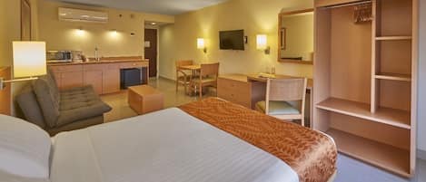 Habitación de hotel con cama, escritorio, sillón, sofá, televisor y armario.