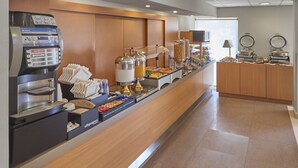 Montaje de bufé con una máquina de café, varios recipientes de comida y una barra con servilletas.