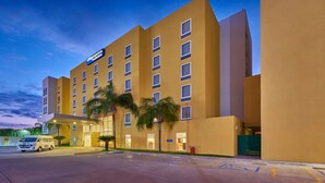 Un hotel moderno con fachada plana, varias ventanas y un estacionamiento con una furgoneta.