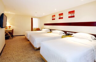Una habitación de hotel con tres camas individuales, un escritorio con lámpara, una silla y una televisión.