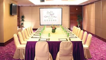 Una sala conferenze con un lungo tavolo, sedie e uno schermo proiettore che mostra 'Casa Real Hotel'.