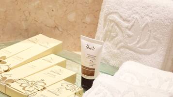 A bathroom with a white towel, a bottle of lotion, and a set of toiletries on a glass shelf.