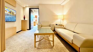 Una habitación de hotel moderna con sofá, una mesa de centro de vidrio, un televisor montado en la pared y una alfombra estampada.