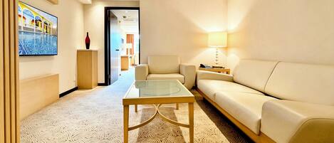 Una habitación de hotel moderna con sofá, una mesa de centro de vidrio, un televisor montado en la pared y una alfombra estampada.
