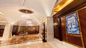 Un hall d’entrée luxueux, avec un sol en marbre, un lustre et un grand panneau décoratif.