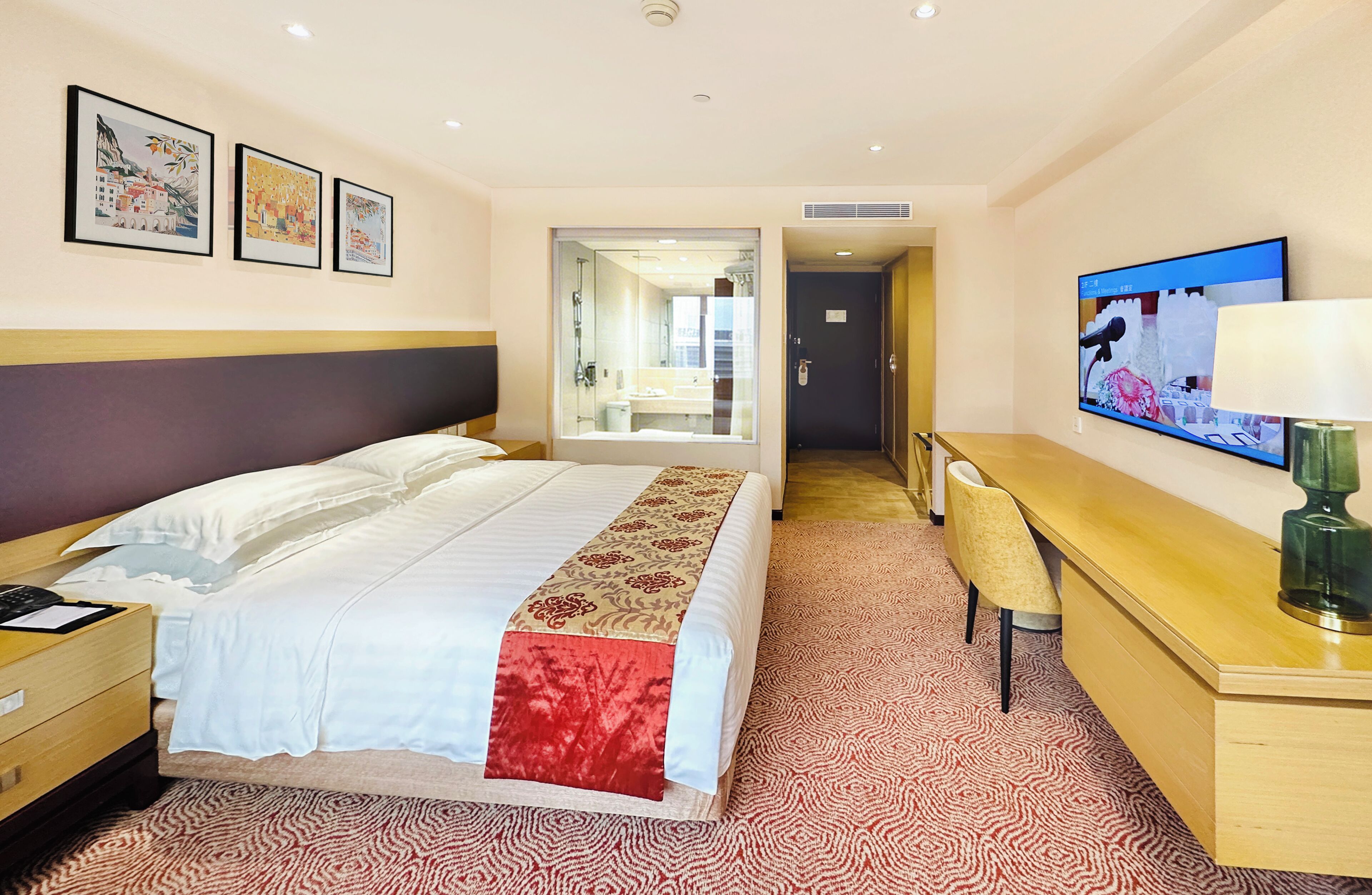 Une chambre d’hôtel avec un lit, un bureau, une chaise, une télévision et une salle de bain visible à travers une porte ouverte.