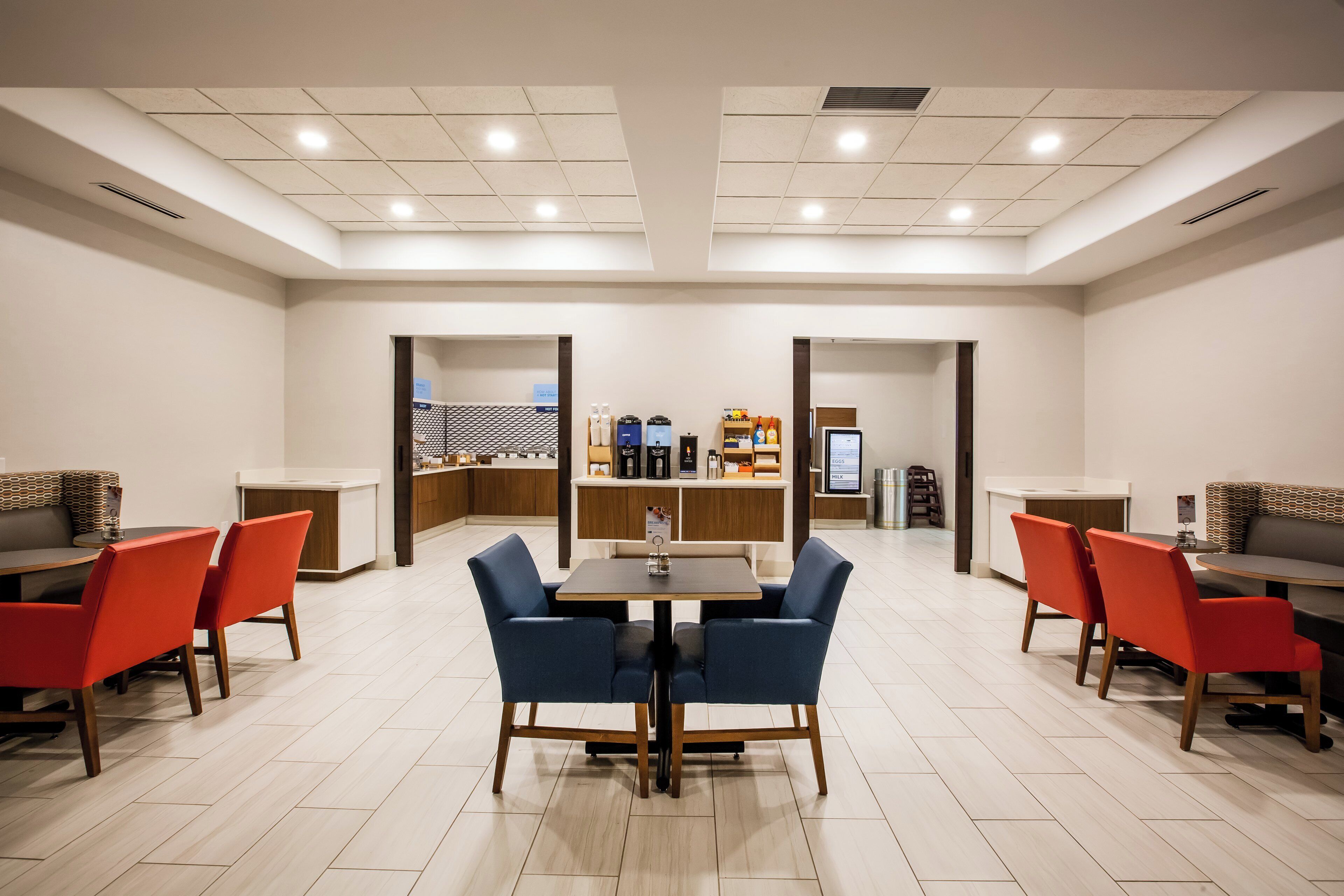 A spacious dining area with a central table surrounded by chairs, a coffee station, and a refrigerator displaying menu items.