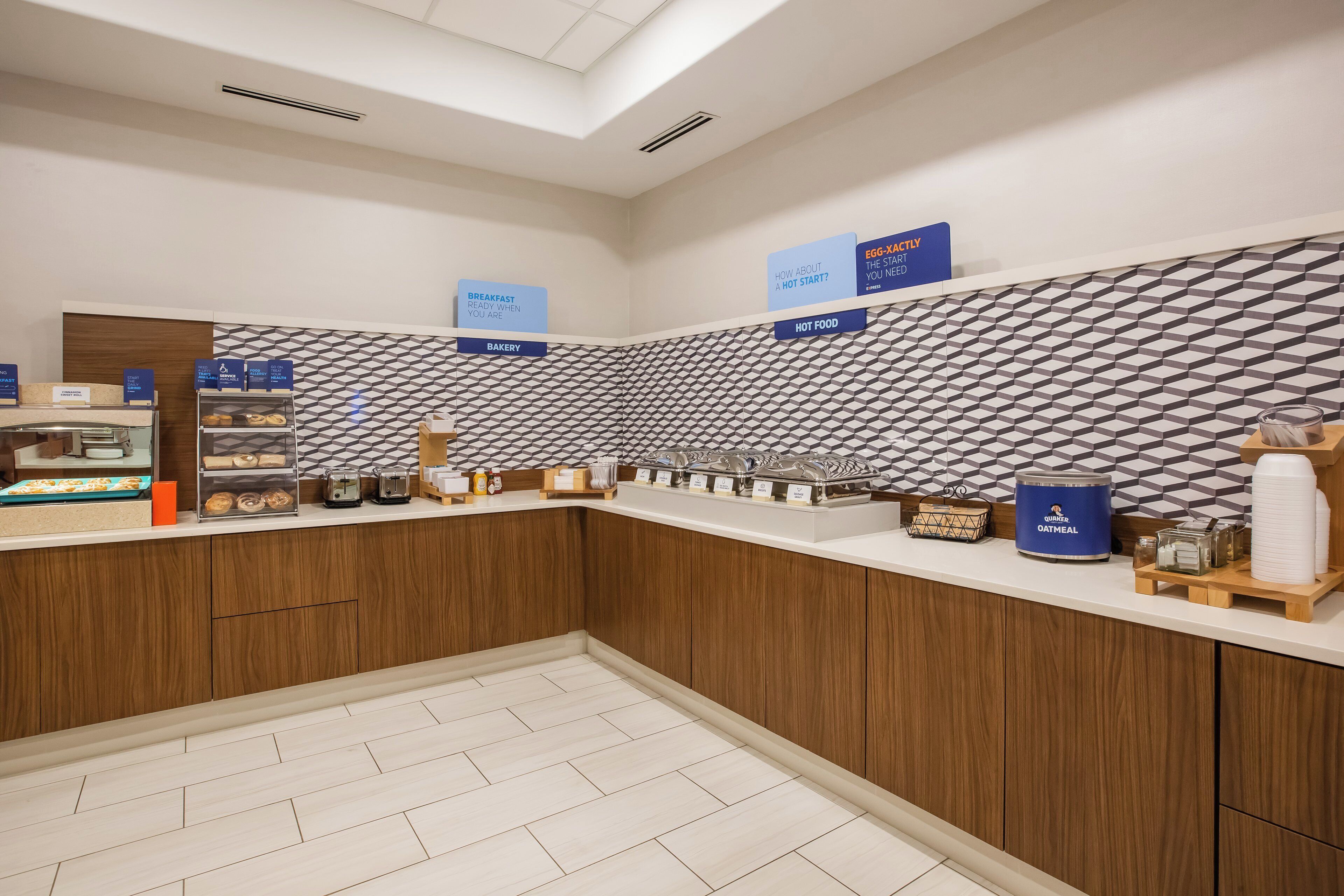 A breakfast area with a counter displaying various food items and a sign indicating a bakery section.