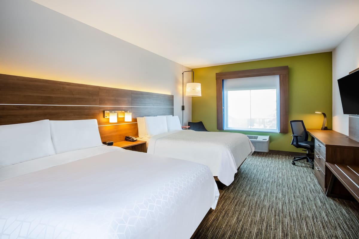 A hotel room with two beds, a desk, a chair, a TV, and a window with a view.