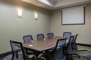 Un salón de conferencias con una mesa larga, seis sillas, una pantalla de proyector y dos luces instaladas en la pared.