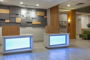 A reception area with two illuminated reception desks, a wall-mounted information board, and a green chair. - Holiday Inn Express Hotel & Suites Fairburn by IHG (Fairburn)