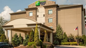 Edificio de Holiday Inn Express & Suites con entrada cubierta, fachada de piedra y bandera estadounidense.