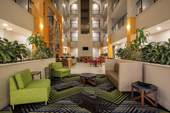 A hotel lobby with a central seating area, multiple tables, and chairs, surrounded by plants and a patterned carpet. - Holiday Inn Express Hotel & Suites Fairburn by IHG (Fairburn)