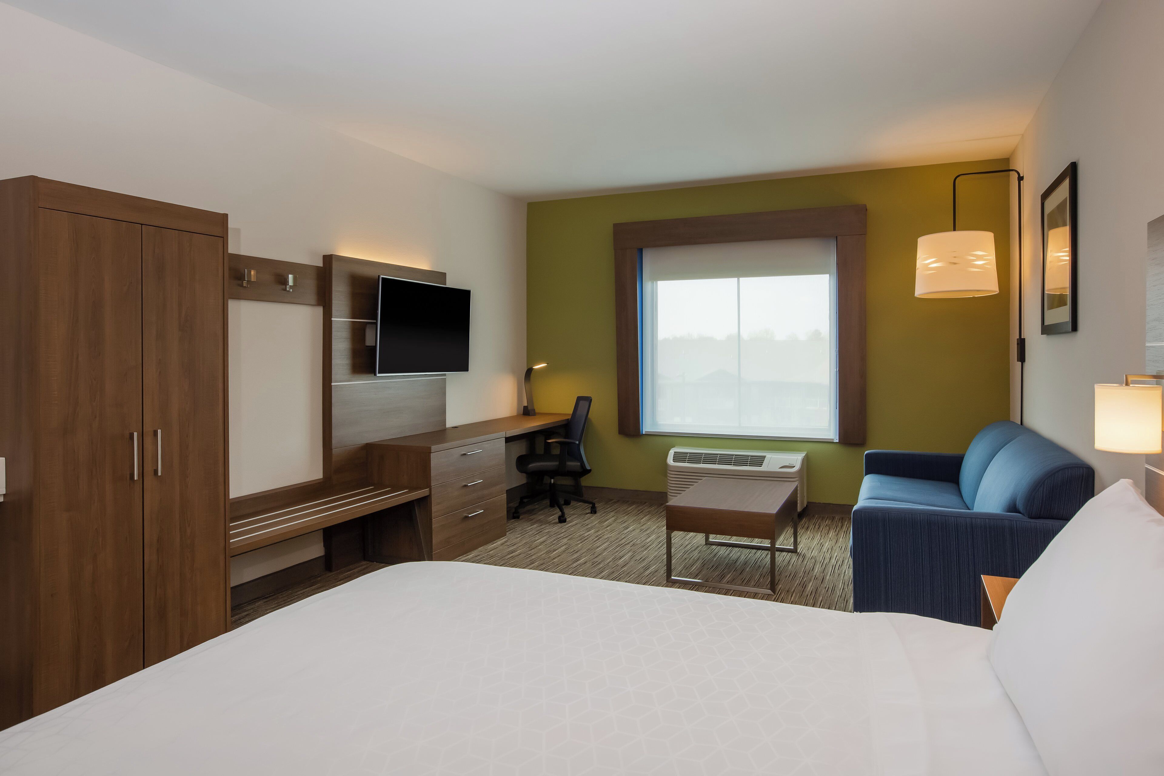 Habitación de hotel con cama, escritorio, silla, televisor, ventana y sofá.