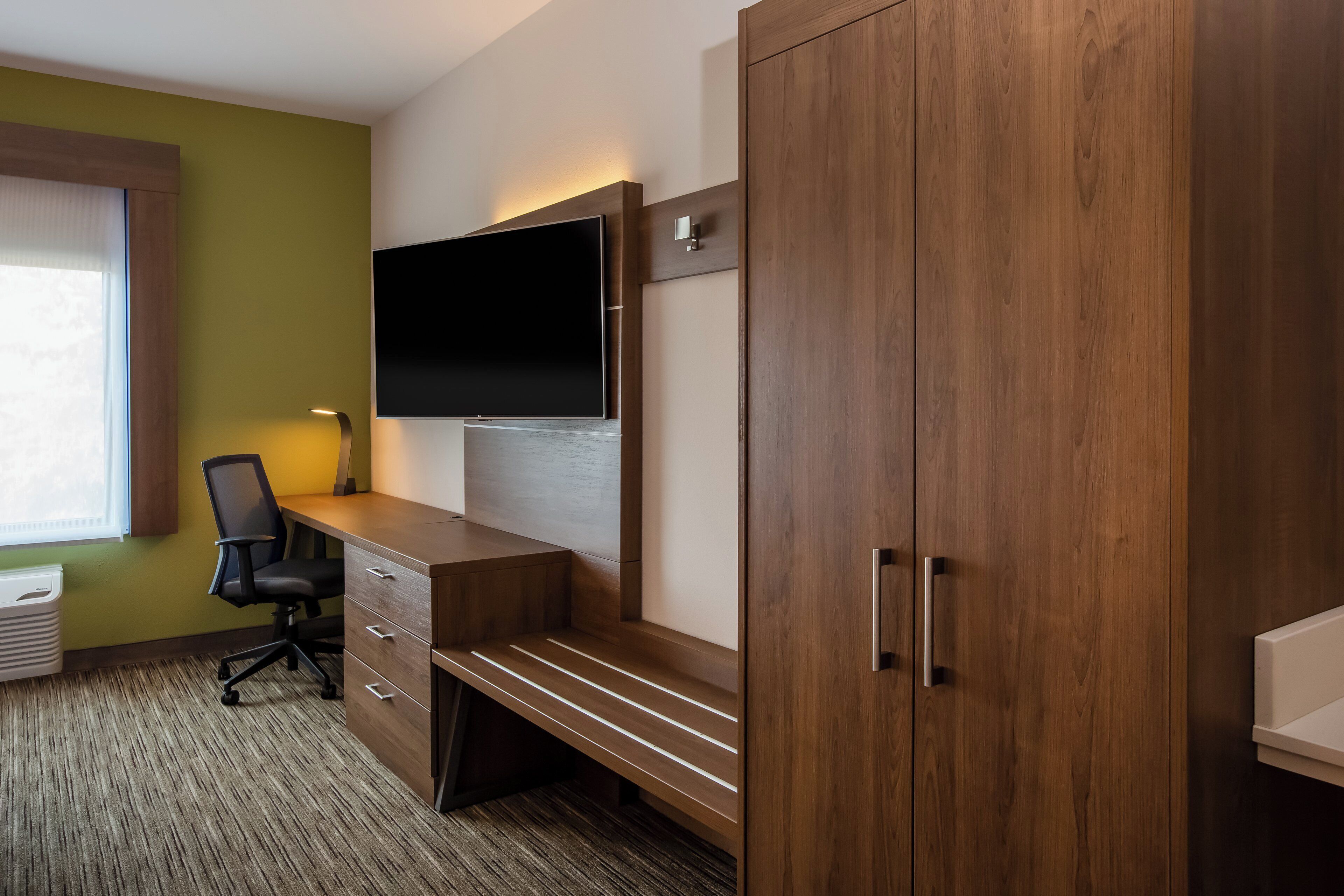 Een hotelkamer met een houten bureau, een flatscreen televisie, een stoel en een kledingkast.