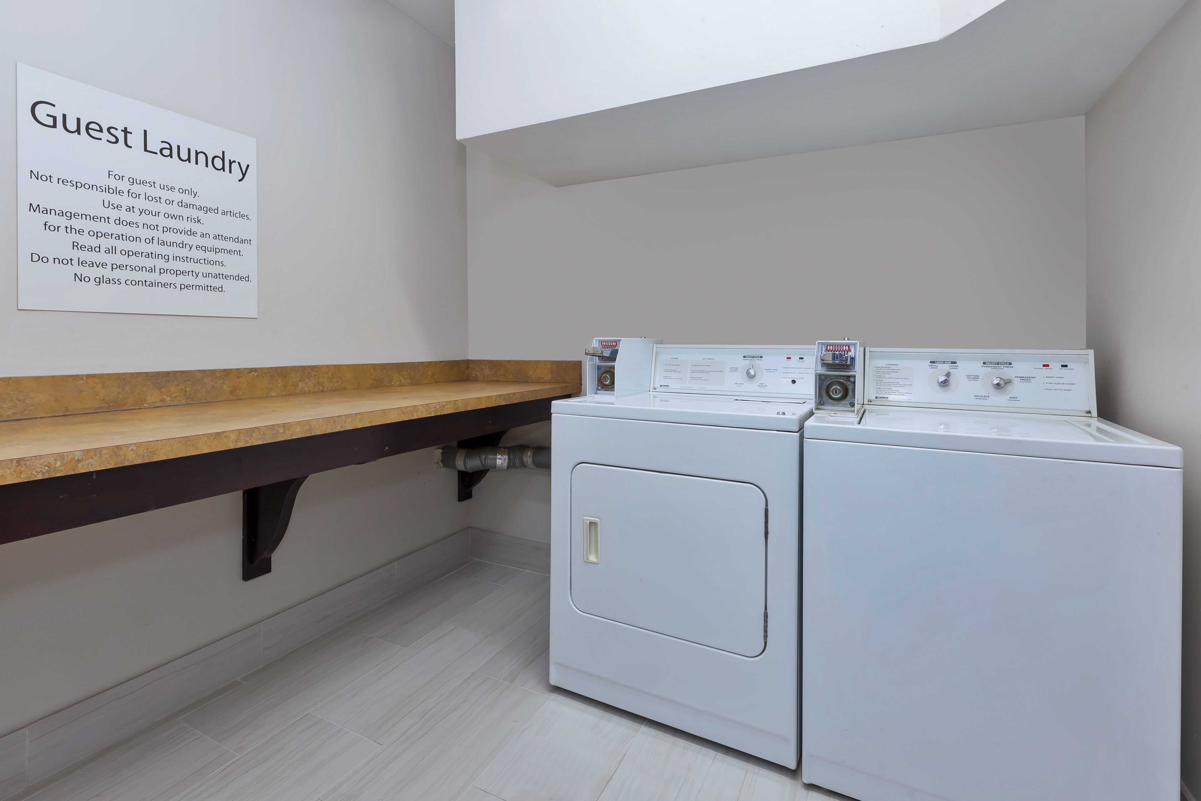 A laundry area with two white washing machines, a wooden counter, and a sign with guest laundry instructions.
