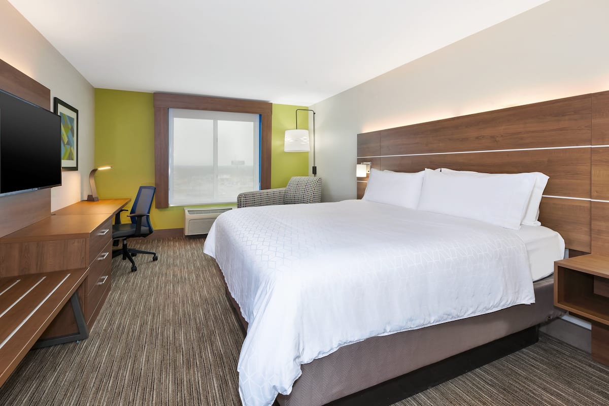 Een hotelkamer met een groot bed, een bureau met stoel, een televisie en een raam met uitzicht over de stad.