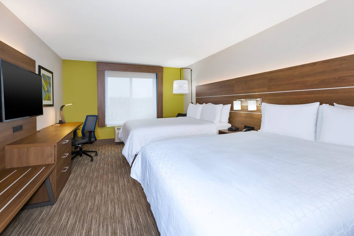 Een hotelkamer met twee bedden, een bureau, een stoel, een televisie en een raam.