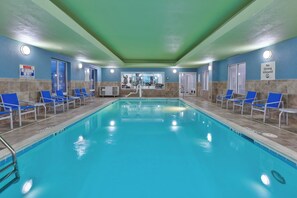 Une piscine intérieure avec des chaises bleues et un panneau indiquant qu’il est interdit de plonger.