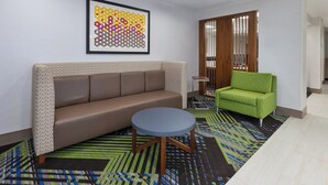 Ein modernes Wohnzimmer mit einer Couch, einem grünen Sessel, einem runden Couchtisch und einem farbenfrohen, abstrakten Gemälde an der Wand.