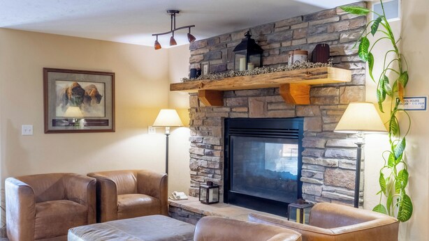 A living room with a stone fireplace, leather sofas, a flat-screen TV, and a potted plant. - Blue Mountain Inn And Suites (Rangely)