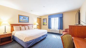 A hotel room with a bed, two bedside tables, a desk, a chair, a flat-screen TV, and a window with curtains.