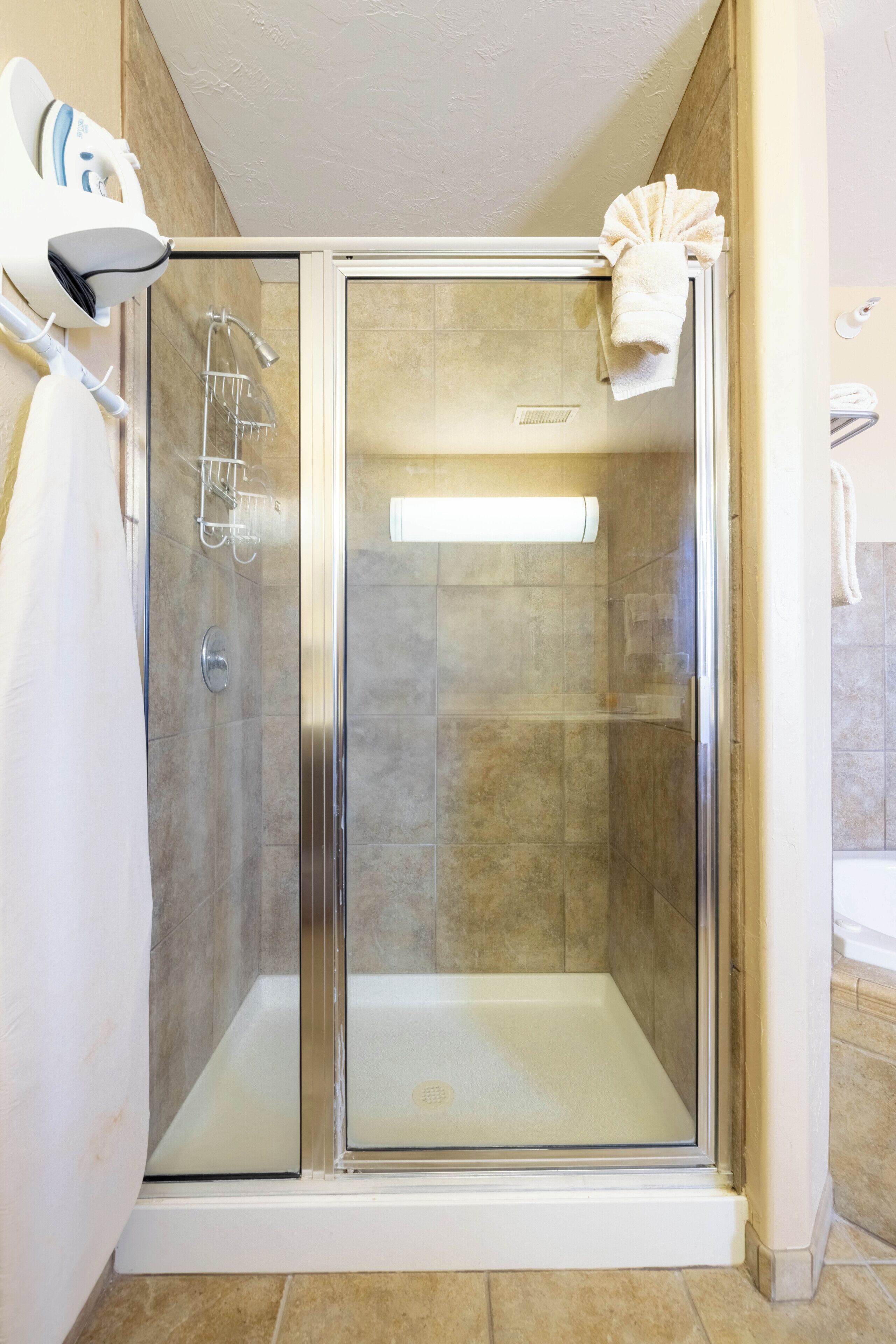 A glass-enclosed shower with a white towel on the door, a towel rack, and a showerhead.