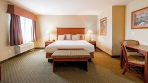 A hotel room with a large bed, bedside lamps, a desk with chairs, and a window with curtains. - Blue Mountain Inn And Suites (Rangely)