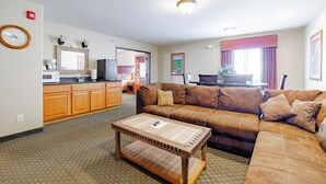 A living room with a sofa, coffee table, kitchen area, and a dining table. - Blue Mountain Inn And Suites (Rangely)
