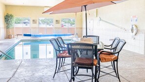 An indoor pool area with a table and chairs, a lifebuoy, and a poolside view. - Blue Mountain Inn And Suites (Rangely)