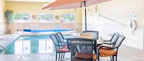 An indoor pool area with a table and chairs, a lifebuoy, and a poolside view.