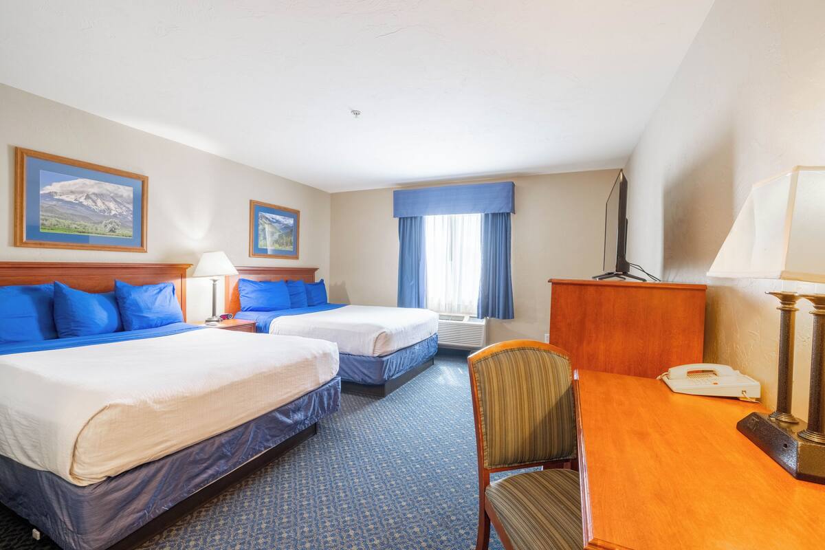 A hotel room with two beds, a desk, a chair, a telephone, and a television.
