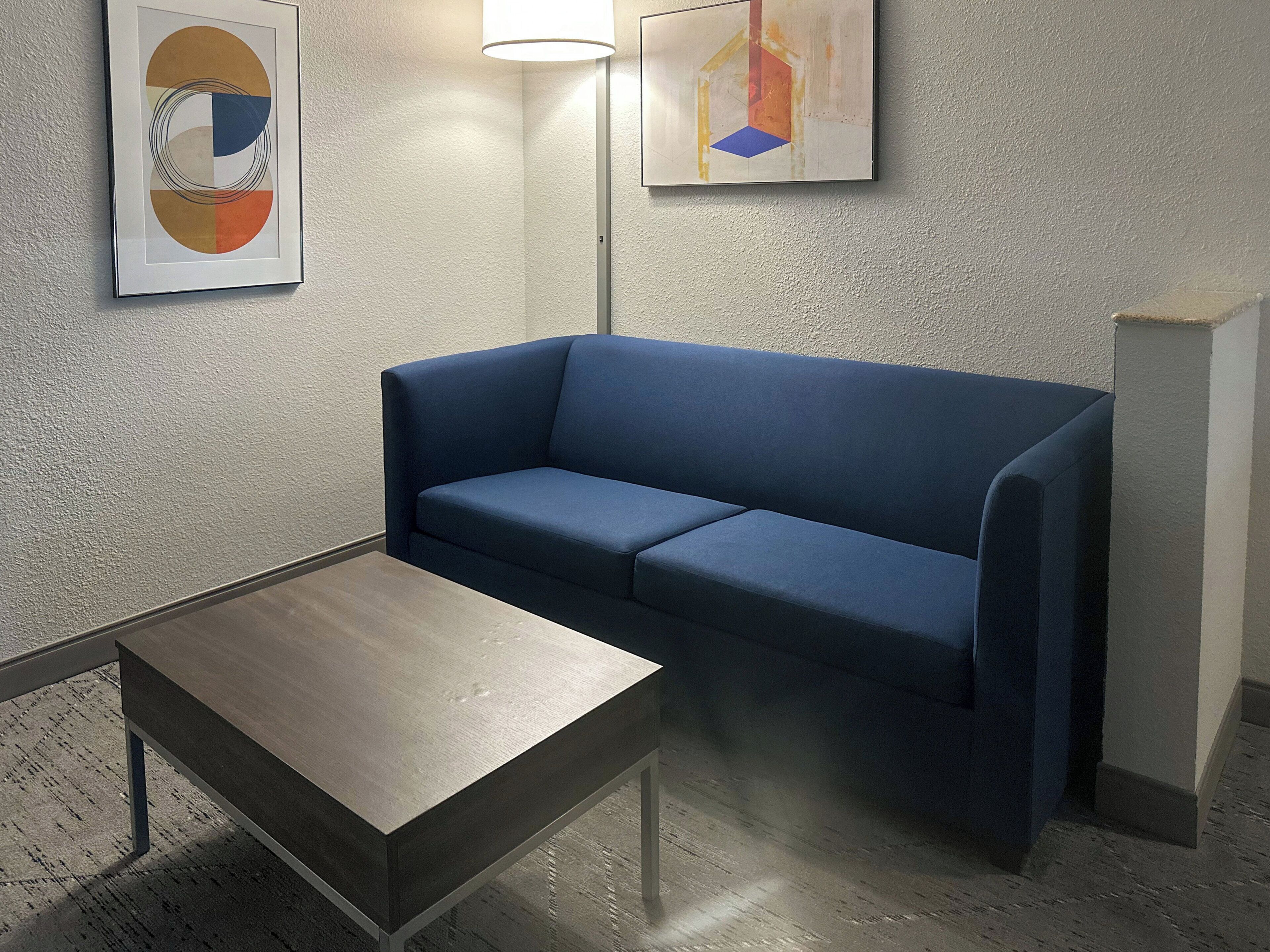 Une pièce avec un canapé bleu, une petite table et deux tableaux abstraits accrochés au mur.